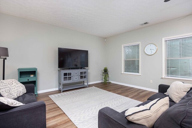 living room with visible vents, a textured ceiling, baseboards, and wood finished floors