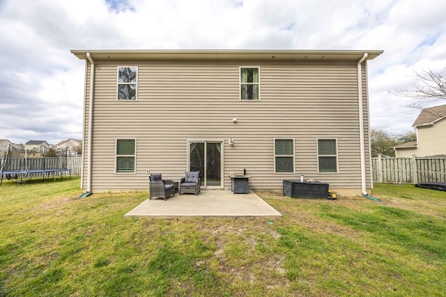 rear view of property featuring a patio, a trampoline, fence, and a lawn