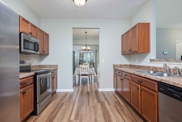 kitchen with a textured ceiling, stainless steel appliances, a sink, light wood-type flooring, and brown cabinetry