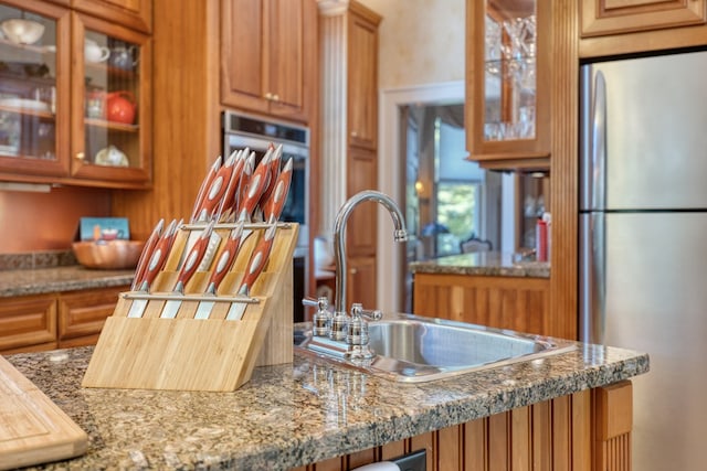 kitchen with light stone counters, sink, and stainless steel fridge