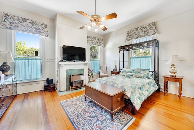 bedroom with multiple windows, hardwood / wood-style flooring, a fireplace, and ceiling fan