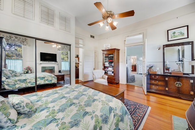 bedroom featuring ceiling fan, a towering ceiling, a premium fireplace, and light wood-type flooring