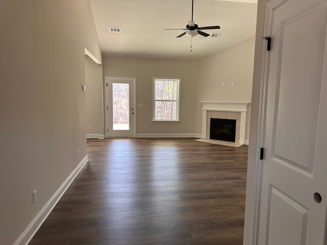 unfurnished living room featuring dark wood-type flooring, a ceiling fan, visible vents, and a tile fireplace