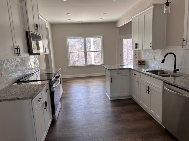 kitchen with a sink, light stone counters, a peninsula, stainless steel appliances, and dark wood-style flooring