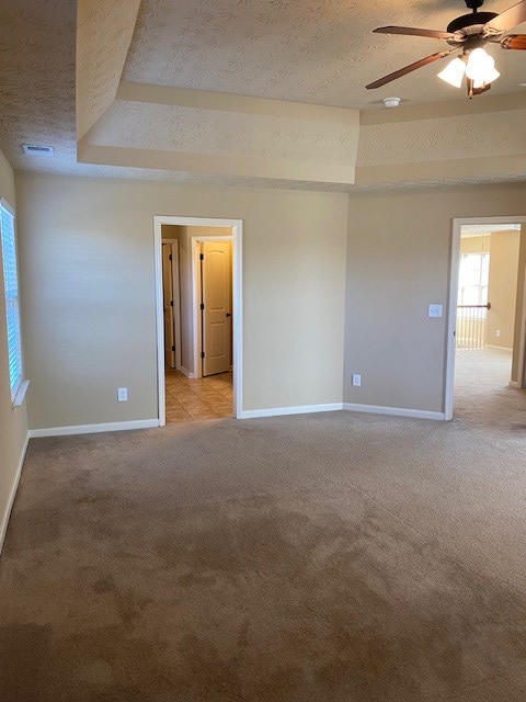 empty room featuring light colored carpet, a textured ceiling, ceiling fan, and a raised ceiling