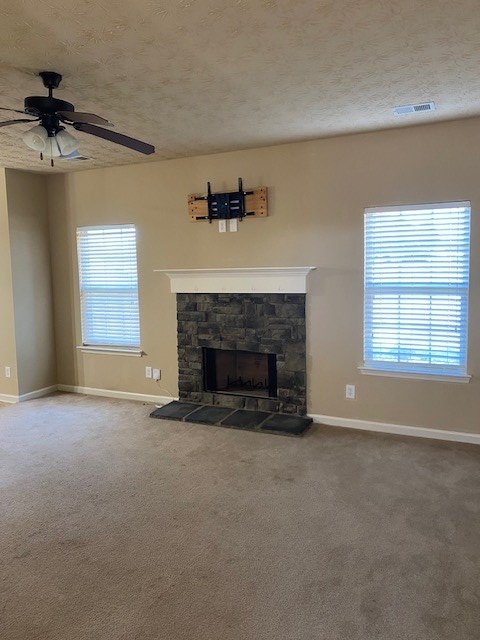 unfurnished living room with ceiling fan, carpet, a textured ceiling, and a stone fireplace