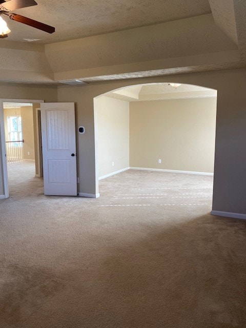 carpeted empty room with lofted ceiling, a textured ceiling, ceiling fan, and a raised ceiling