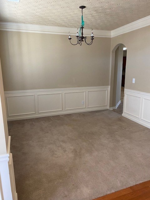 carpeted empty room featuring a textured ceiling, crown molding, and a notable chandelier