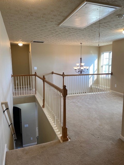 staircase with a textured ceiling, a chandelier, and carpet flooring