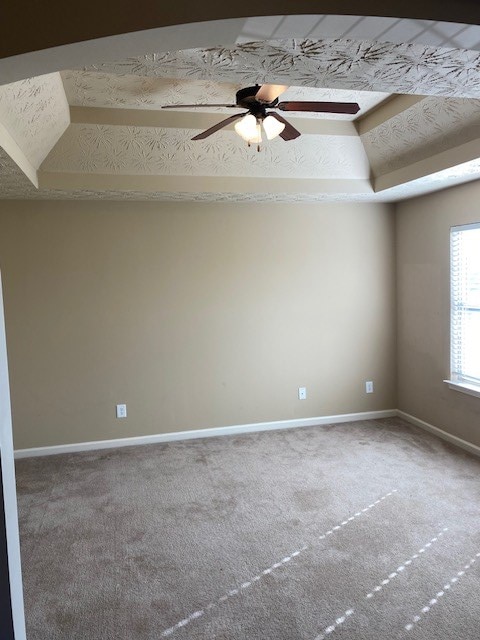 carpeted spare room with ceiling fan and a raised ceiling