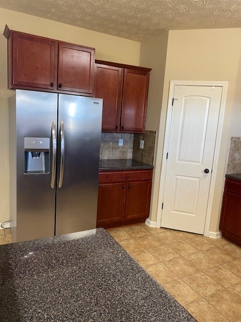 kitchen with tasteful backsplash, dark stone counters, and stainless steel fridge