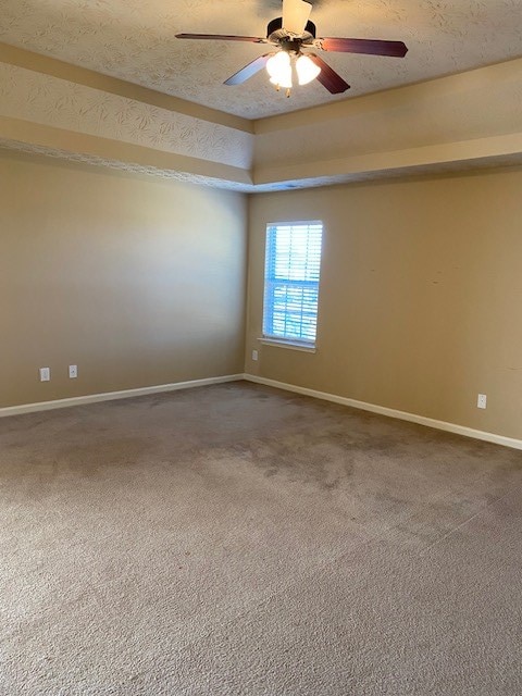 empty room featuring ceiling fan, carpet, a tray ceiling, and a textured ceiling