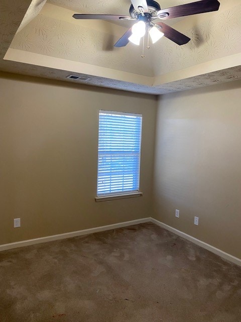 empty room featuring ceiling fan, a raised ceiling, and carpet flooring