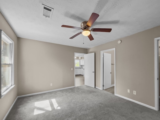 unfurnished bedroom with a textured ceiling, carpet floors, visible vents, and baseboards