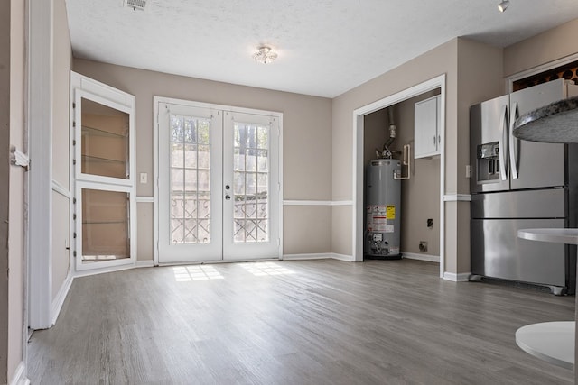 interior space featuring french doors, water heater, a textured ceiling, wood finished floors, and baseboards