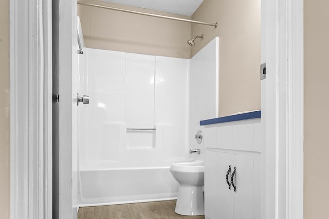 full bath with toilet, a textured ceiling, bathtub / shower combination, and wood finished floors