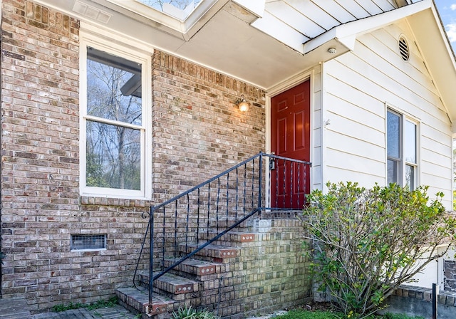 view of exterior entry featuring brick siding and visible vents