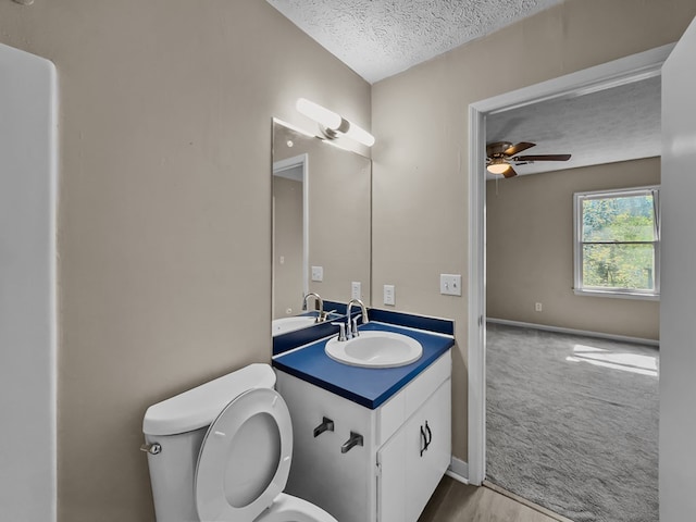 bathroom with toilet, a ceiling fan, a textured ceiling, vanity, and baseboards