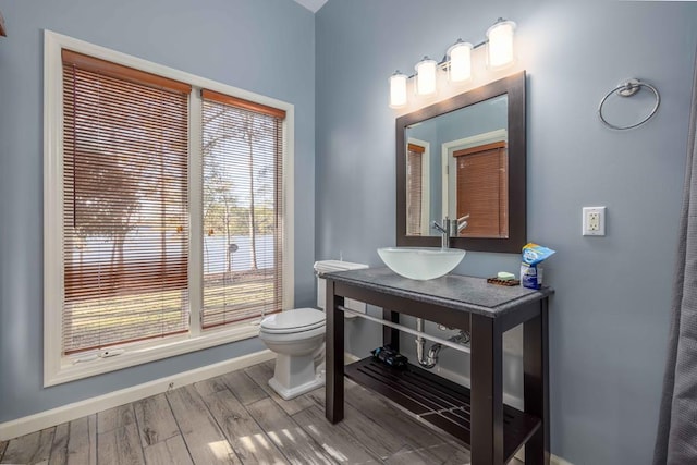 bathroom with toilet, wood finished floors, baseboards, and a sink