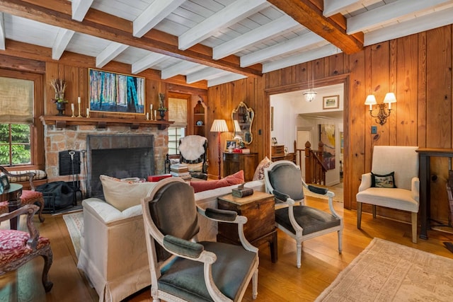 living area with wood walls, beam ceiling, wood finished floors, and a stone fireplace