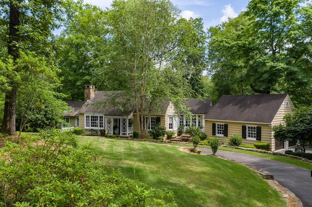 new england style home with driveway, a chimney, and a front yard