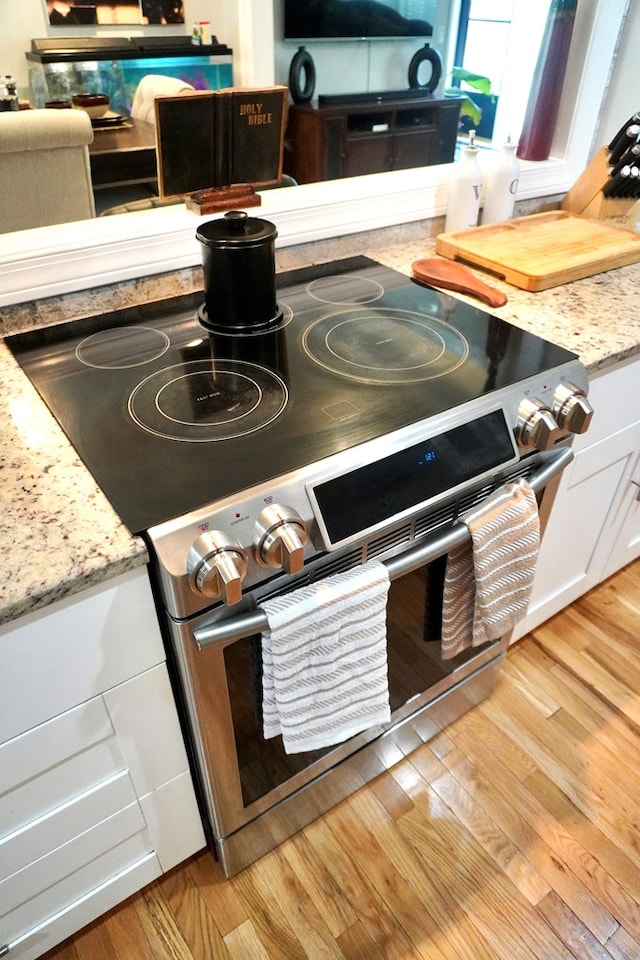 404 19th Ave, Phenix City, AL 36869 - kitchen view of stainless steel electric range, light wood-style flooring, white cabinetry, and light stone counters