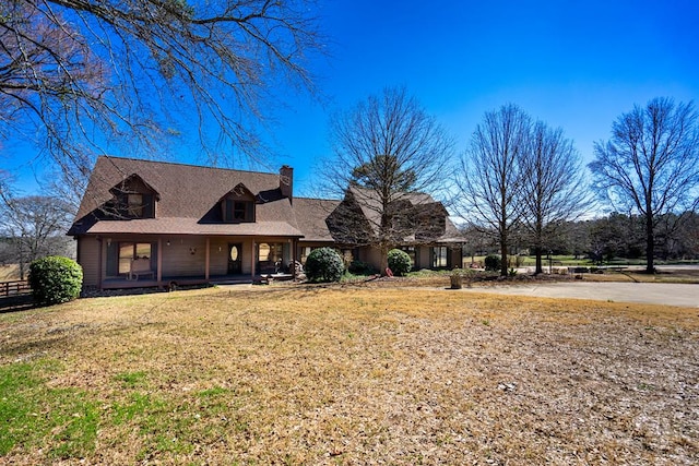 view of front of house featuring a porch, a chimney, and a front lawn