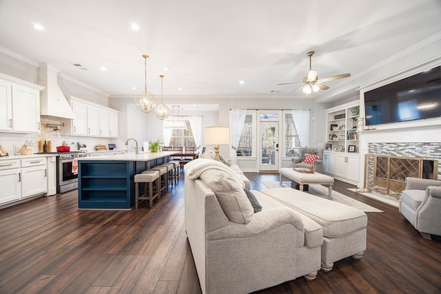 living room featuring a tiled fireplace, ceiling fan with notable chandelier, ornamental molding, and dark hardwood / wood-style floors