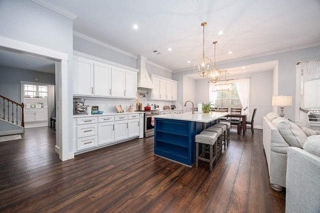 kitchen with an island with sink, premium range hood, stainless steel range with gas stovetop, and white cabinets