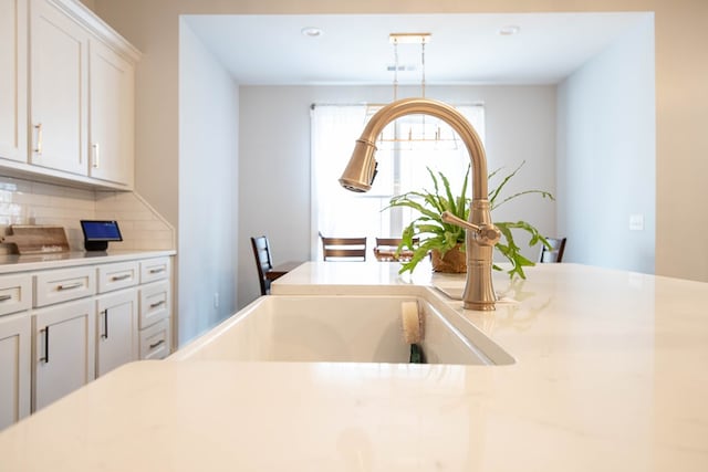 kitchen with white cabinetry, decorative light fixtures, sink, and backsplash