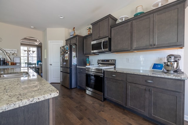 kitchen featuring arched walkways, dark brown cabinetry, stainless steel appliances, a sink, and backsplash