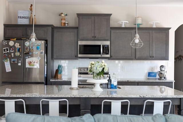 kitchen featuring a breakfast bar area, dark brown cabinets, appliances with stainless steel finishes, backsplash, and pendant lighting