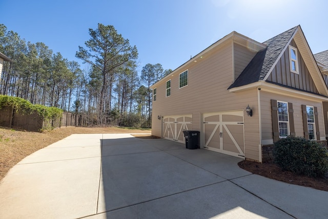 view of side of property with a garage, concrete driveway, board and batten siding, and roof with shingles