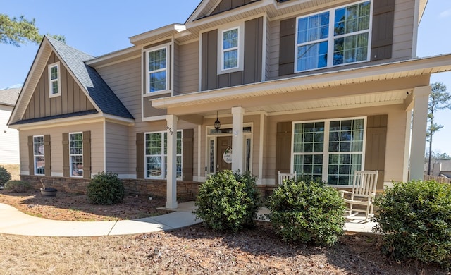 craftsman inspired home featuring board and batten siding, covered porch, roof with shingles, and stone siding