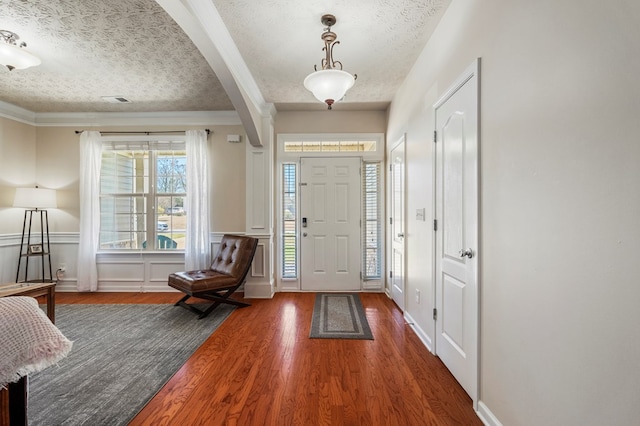 entryway with wainscoting, wood finished floors, arched walkways, a decorative wall, and a textured ceiling