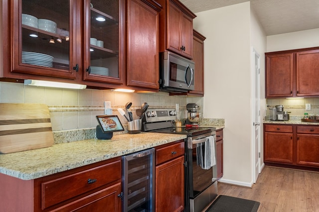 kitchen featuring light stone countertops, beverage cooler, light wood-style flooring, decorative backsplash, and appliances with stainless steel finishes