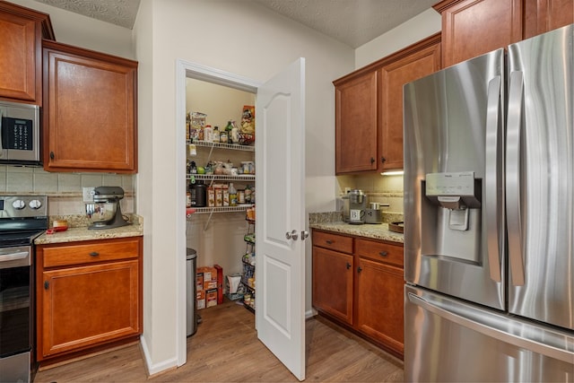 kitchen with light wood finished floors, backsplash, appliances with stainless steel finishes, and a textured ceiling