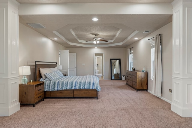 bedroom with visible vents, light colored carpet, a tray ceiling, and decorative columns