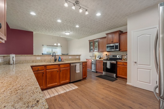 kitchen with light wood-type flooring, a sink, stainless steel appliances, a peninsula, and brown cabinetry