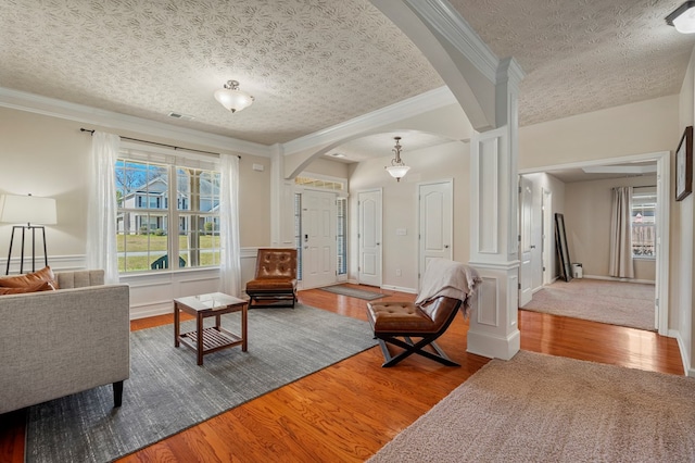 living area with wood finished floors, visible vents, arched walkways, a textured ceiling, and crown molding