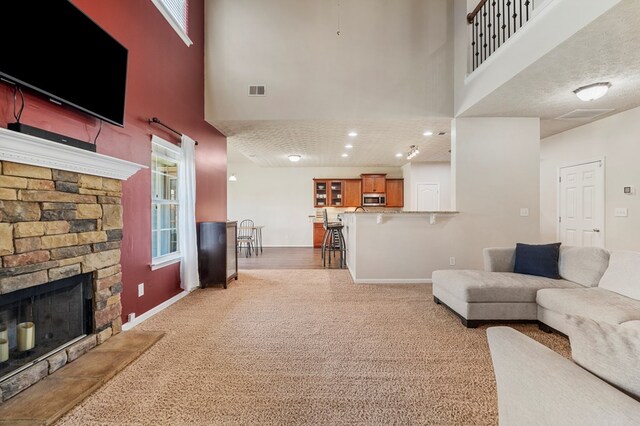 living area featuring a stone fireplace, visible vents, baseboards, and carpet