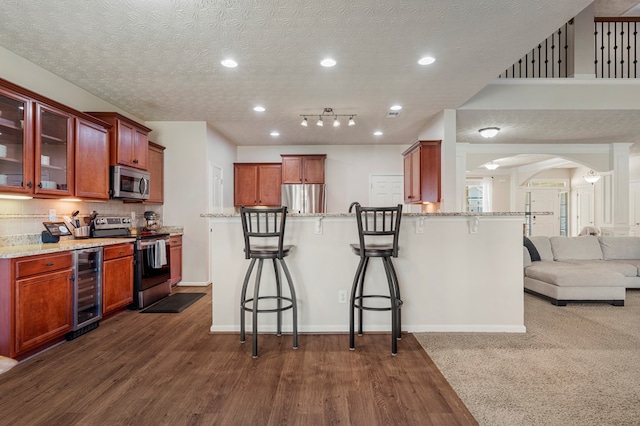 kitchen featuring arched walkways, stainless steel appliances, wine cooler, glass insert cabinets, and a kitchen breakfast bar