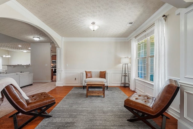 living area featuring a textured ceiling, wood finished floors, arched walkways, wainscoting, and crown molding