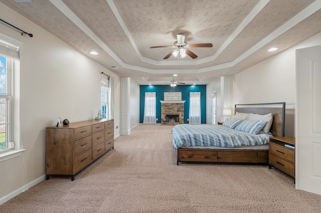 bedroom featuring a tray ceiling, light carpet, multiple windows, and a fireplace