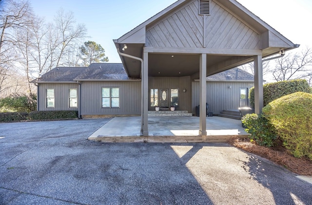 back of house with a shingled roof, a carport, and a patio