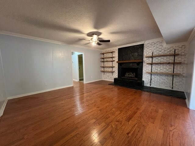 unfurnished living room featuring hardwood / wood-style flooring, crown molding, a brick fireplace, and a textured ceiling