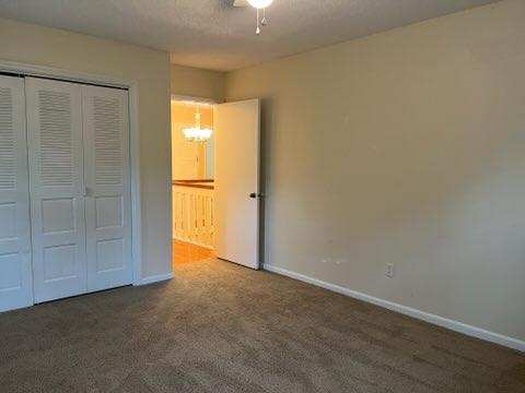 unfurnished bedroom with dark carpet, an inviting chandelier, and a closet