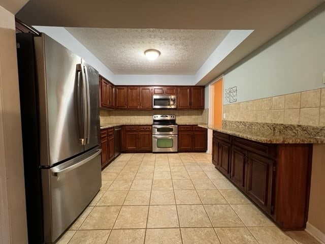 kitchen with backsplash, light stone counters, light tile patterned floors, and stainless steel appliances