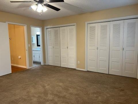 unfurnished bedroom featuring ensuite bathroom, dark carpet, ceiling fan, white refrigerator, and multiple closets