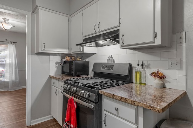 kitchen featuring gas range, black microwave, baseboards, white cabinets, and under cabinet range hood